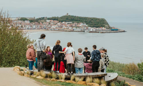 A group of people stand next to a bench on a cliff overlooking the sea in Scarborough