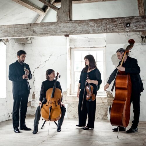 Quartet participants holding their instruments in a rustic looking room