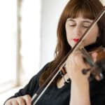 A woman in black concert dress play a violin in a room with white walls
