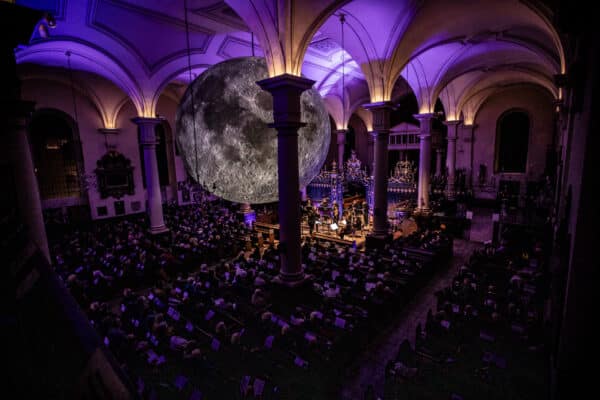 Sinfonia Viva orchestra playing to a crowd in purple lighting with a big planet installation above them