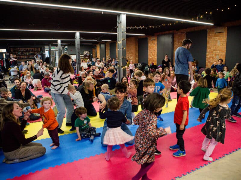 Group of children and adults dancing and playing on brightly coloured mats