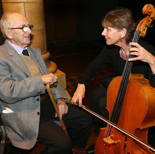 A cellist performs up close to an elderly man.