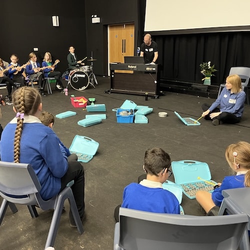A class plays a variety of musical instruments including ukulele and drums, supporting by Sinfonia Viva workshop leaders