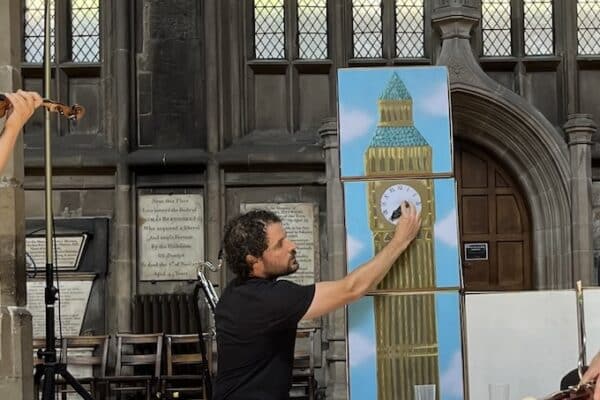 A violinist plays while another performer toys with a prop representing Big Ben