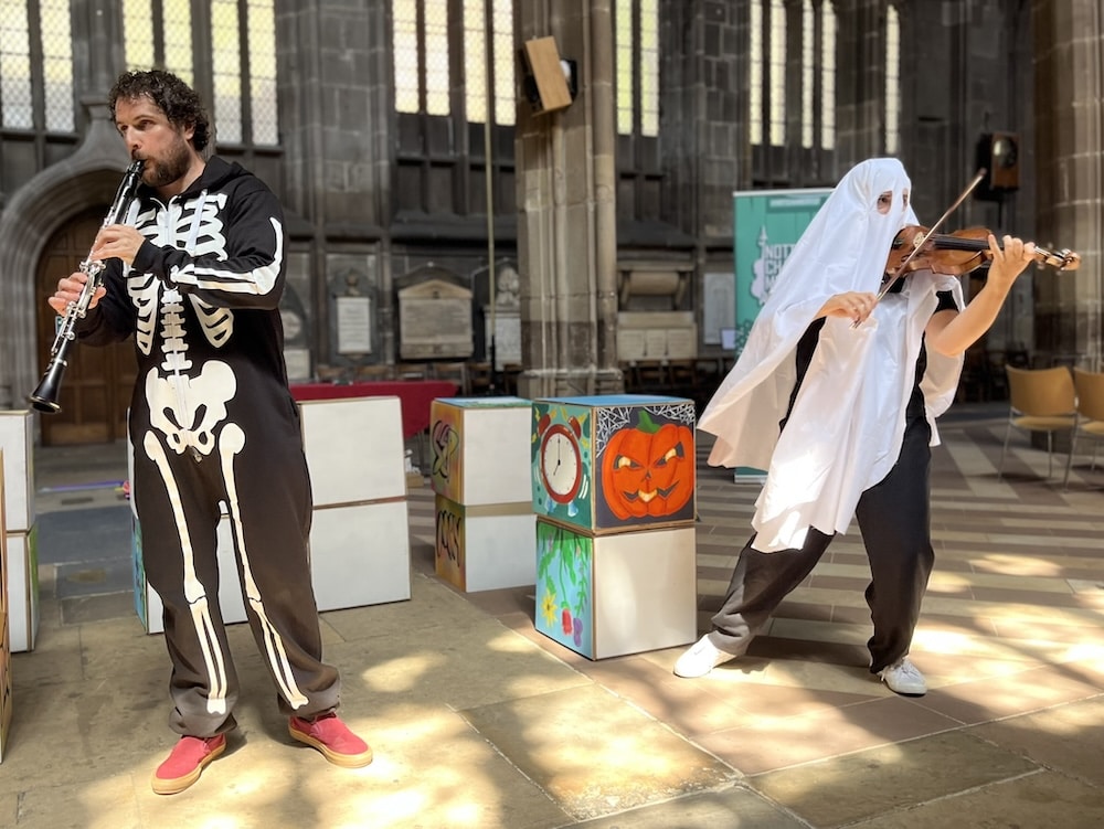 A clarinet player and a violinist are dressed in Hallowe'en costumes, performing in a church